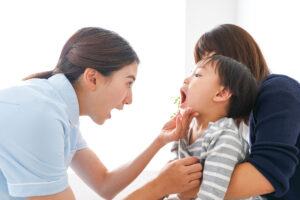 母親の膝の上に座って口を開ける少年と口の中を確認する女性歯科医師