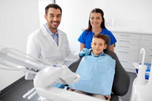 歯科の椅子に座る男の子の横に歯科医師・歯科助手がいる
